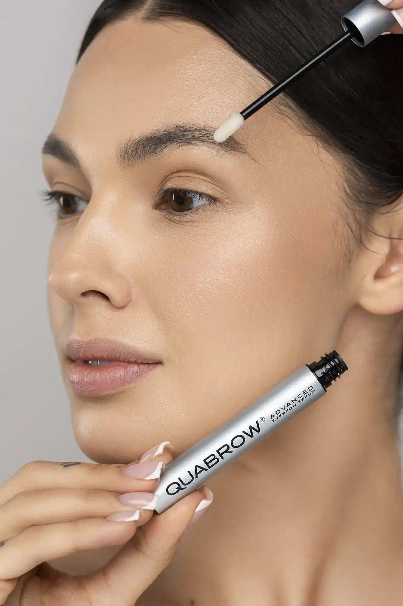 Woman holding QUABROW Advanced Eyebrow Serum and smiling after application – Step 2